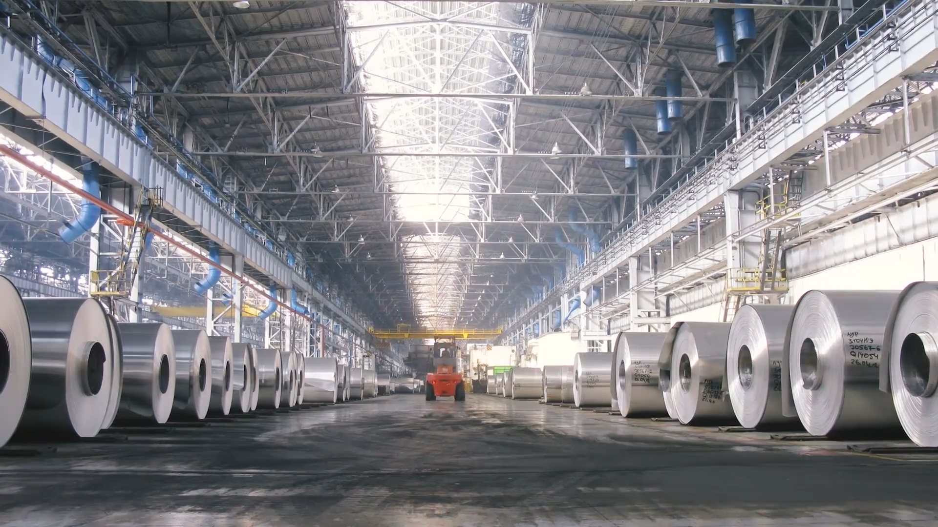 A forklift moving between rows of aluminium coils on the floor of a manufacturing plant